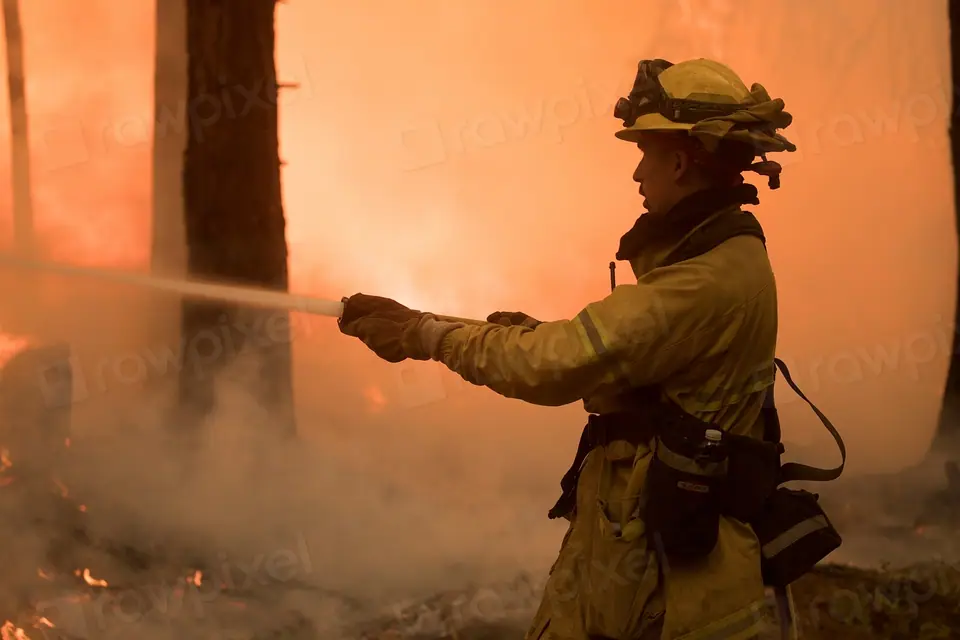 Bombero forestal rociando agua directamente sobre las llamas, con vapor subiendo