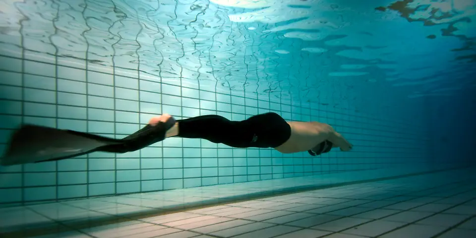 Apneísta con monoaleta nadando bajo el agua en una piscina