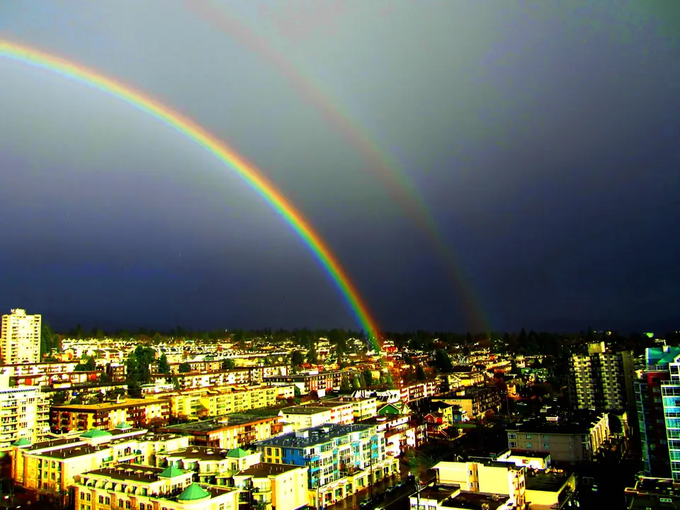 Arcoíris doble sobre una ciudad: el arco principal es brillante, el secundario más tenue, y el cielo entre los dos es más oscuro