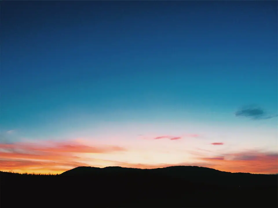 Cielo al atardecer: azul arriba, que pasa a naranja y rojo cerca del horizonte, sobre la silueta oscura de unas colinas