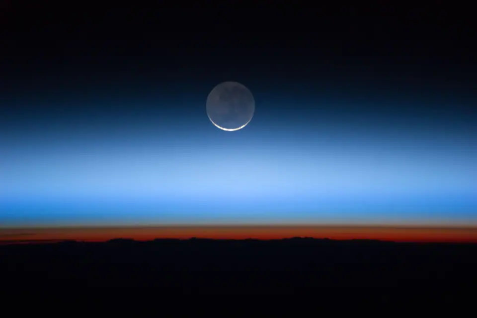La Luna sobre el horizonte terrestre visto desde la Estación Espacial, con las capas de la atmósfera en franjas azules y naranjas