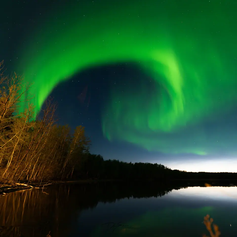 Aurora boreal verde en forma de espiral sobre un lago y un bosque, de noche