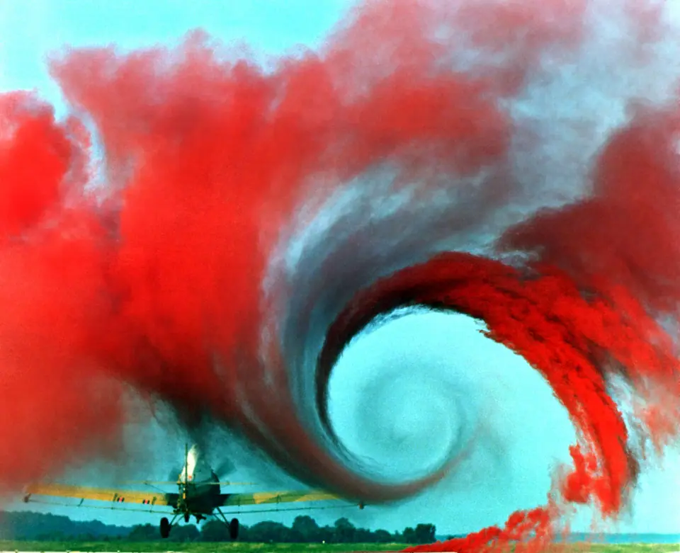 Un avión pasa volando bajo sobre humo de colores: el aire que empuja el ala hacia abajo deja un gran remolino en la punta