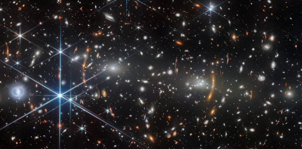 Cúmulo de galaxias con arcos de luz distorsionada por lente gravitacional: cada galaxia se aleja de las demás a medida que el espacio entre ellas se expande
