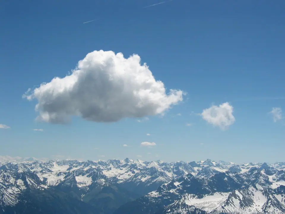 Una nube cúmulo aislada, blanca y algodonosa, flota sobre una cordillera nevada con cielo azul