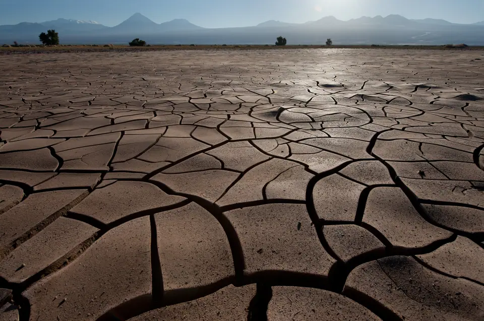 Suelo de desierto reseco y agrietado, con montañas al fondo
