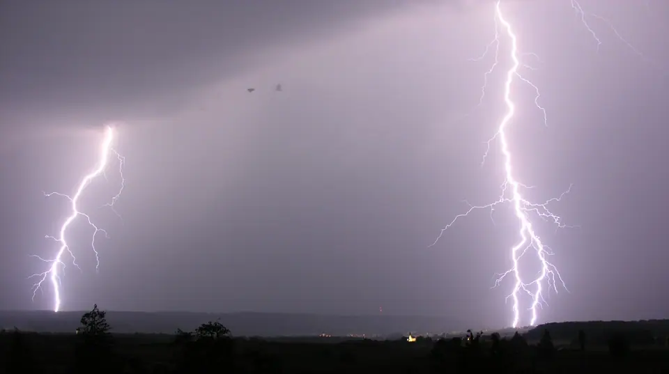 Dos rayos caen al mismo tiempo sobre una llanura bajo una tormenta, uno cerca y otro a lo lejos