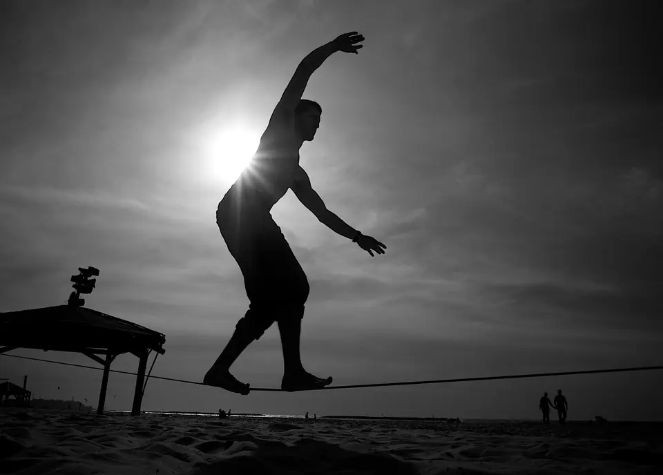 Silueta de una persona que camina sobre una cinta de slackline en la playa, con los brazos abiertos para mantener el equilibrio
