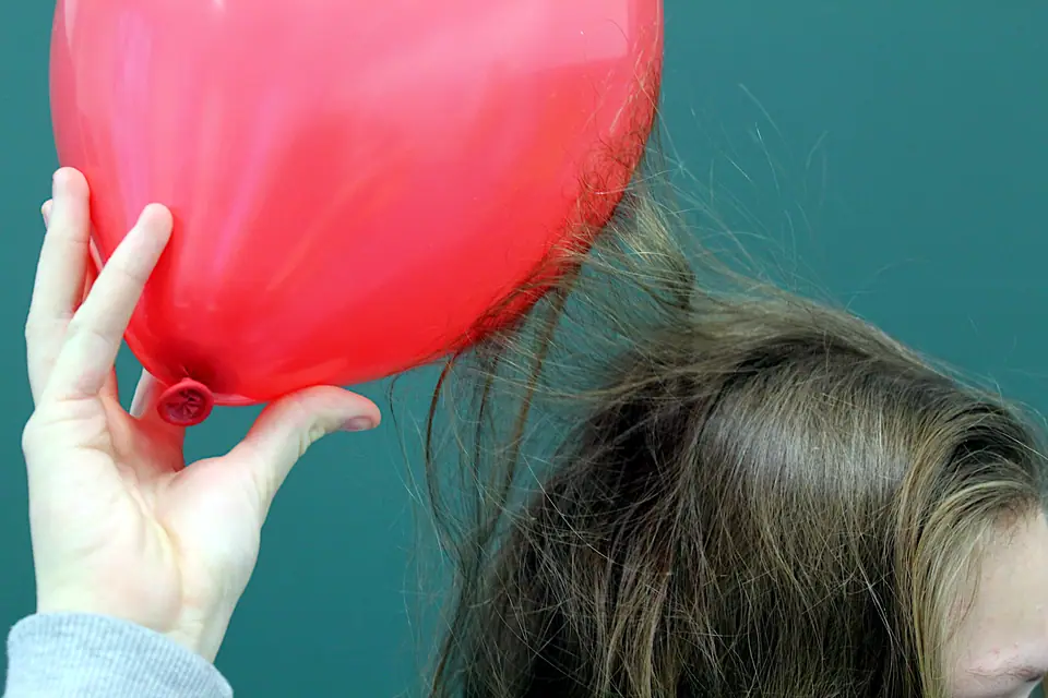 Una mano sostiene un globo rojo cerca de una cabeza y el pelo se levanta hacia el globo, atraído por la carga eléctrica
