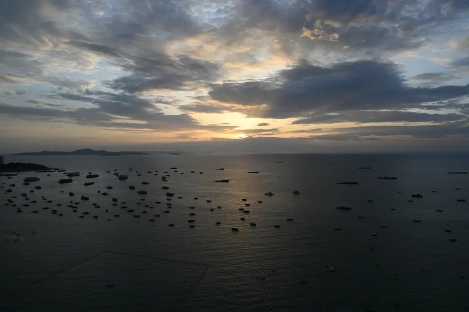 Mar en calma al atardecer, con la línea del horizonte recta y barcos pequeños recortados sobre el agua