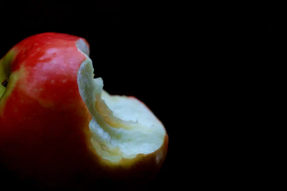 Manzana roja mordida sobre fondo negro, con la pulpa expuesta al aire