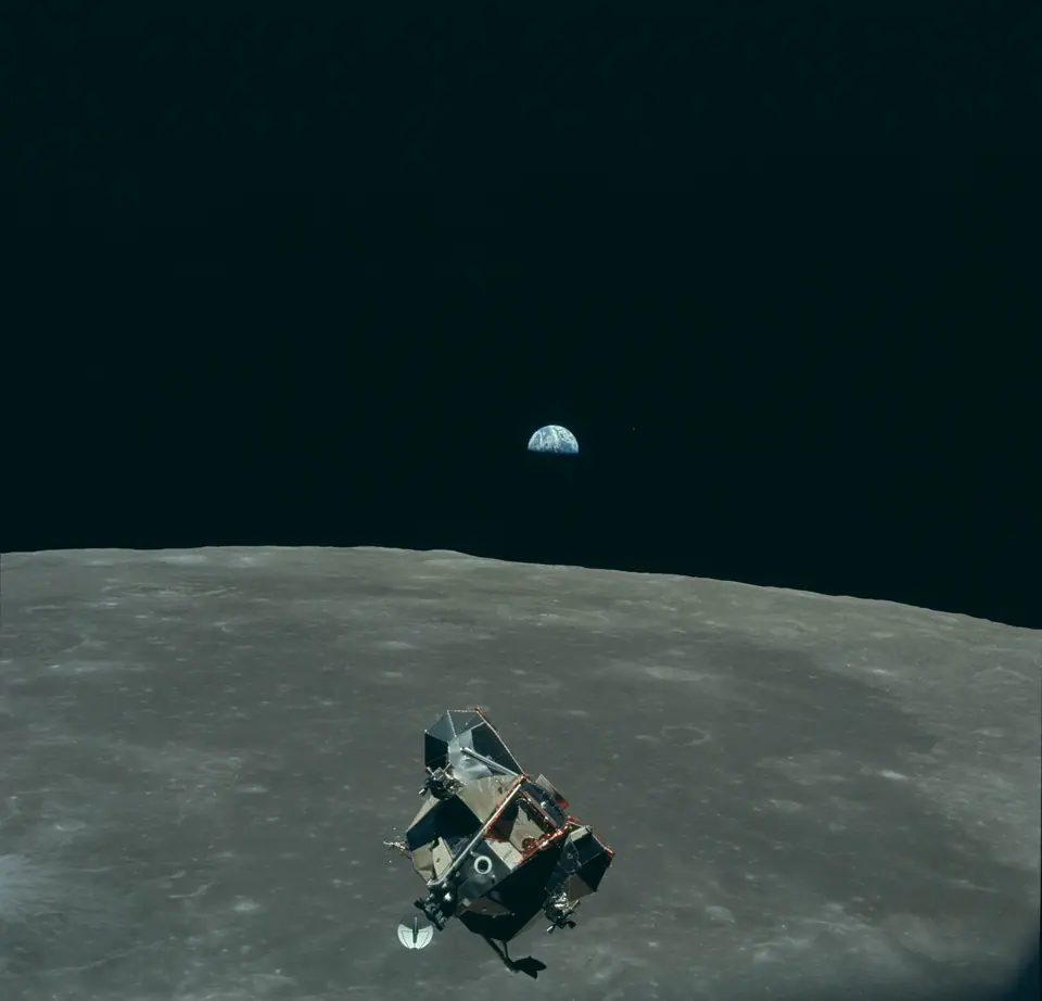 El módulo lunar del Apolo 11 sobre la superficie gris de la Luna, bajo un cielo negro, con la Tierra azul a lo lejos