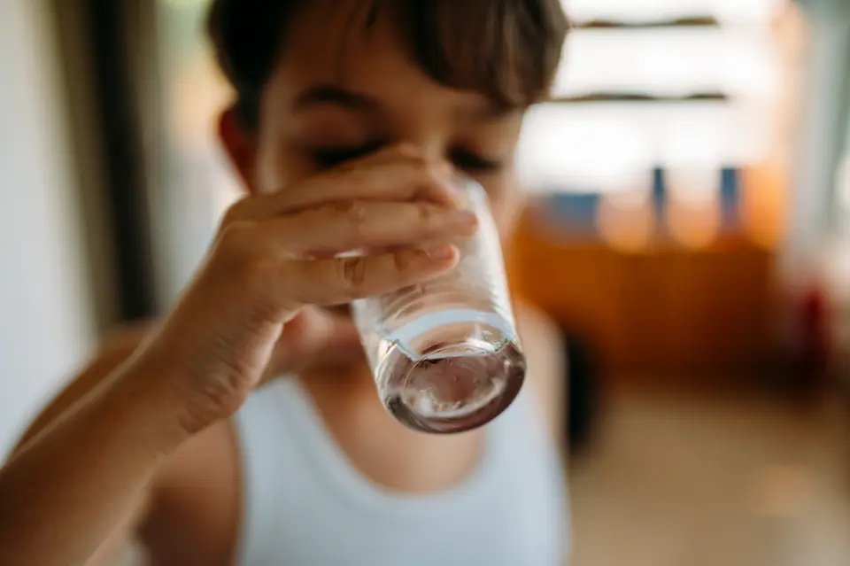 Un niño toma agua de un vaso de vidrio en una casa