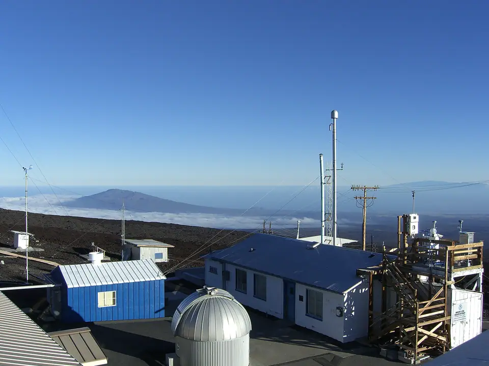 Edificios y torres de medición del Observatorio de Mauna Loa, en Hawái, sobre la lava a 3400 metros, con el Mauna Kea al fondo