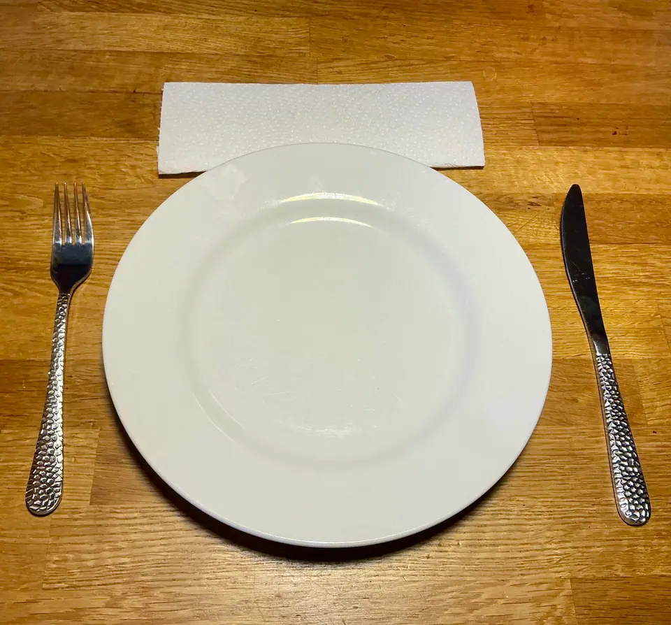 Plato blanco vacío con tenedor y cuchillo sobre una mesa de madera