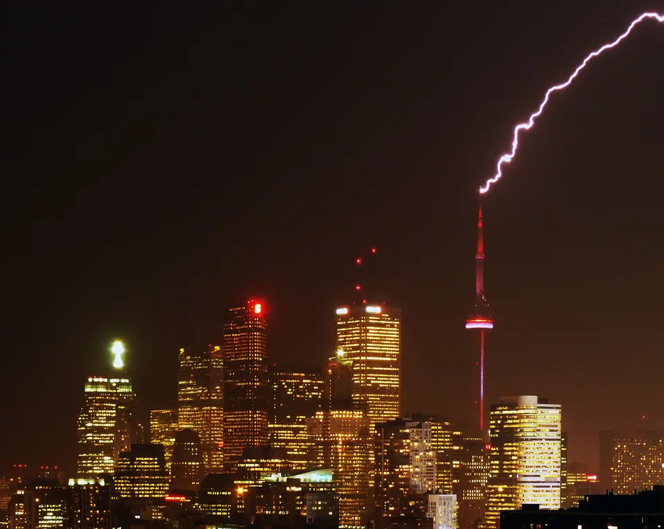 Un rayo cae sobre la punta de la Torre CN de Toronto, de noche, sobre los edificios iluminados del centro