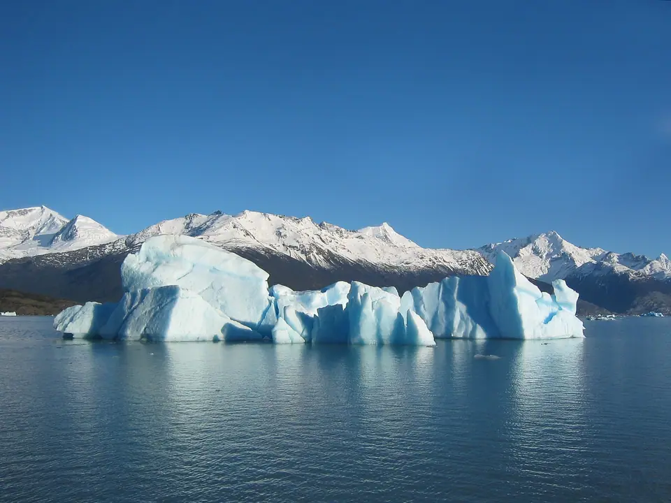 Témpano de hielo azulado flotando en un lago glaciar de la Patagonia argentina, con montañas nevadas al fondo